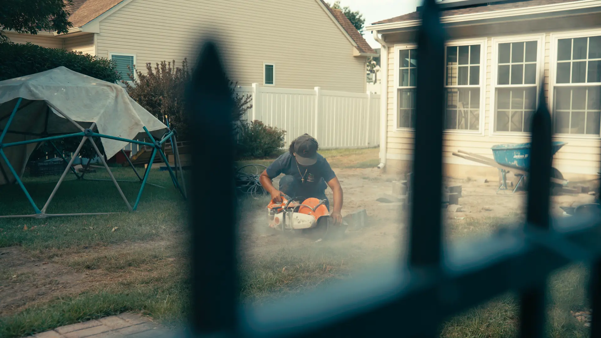 Crew member cutting pavers with a cut-off saw in a fenced backyard