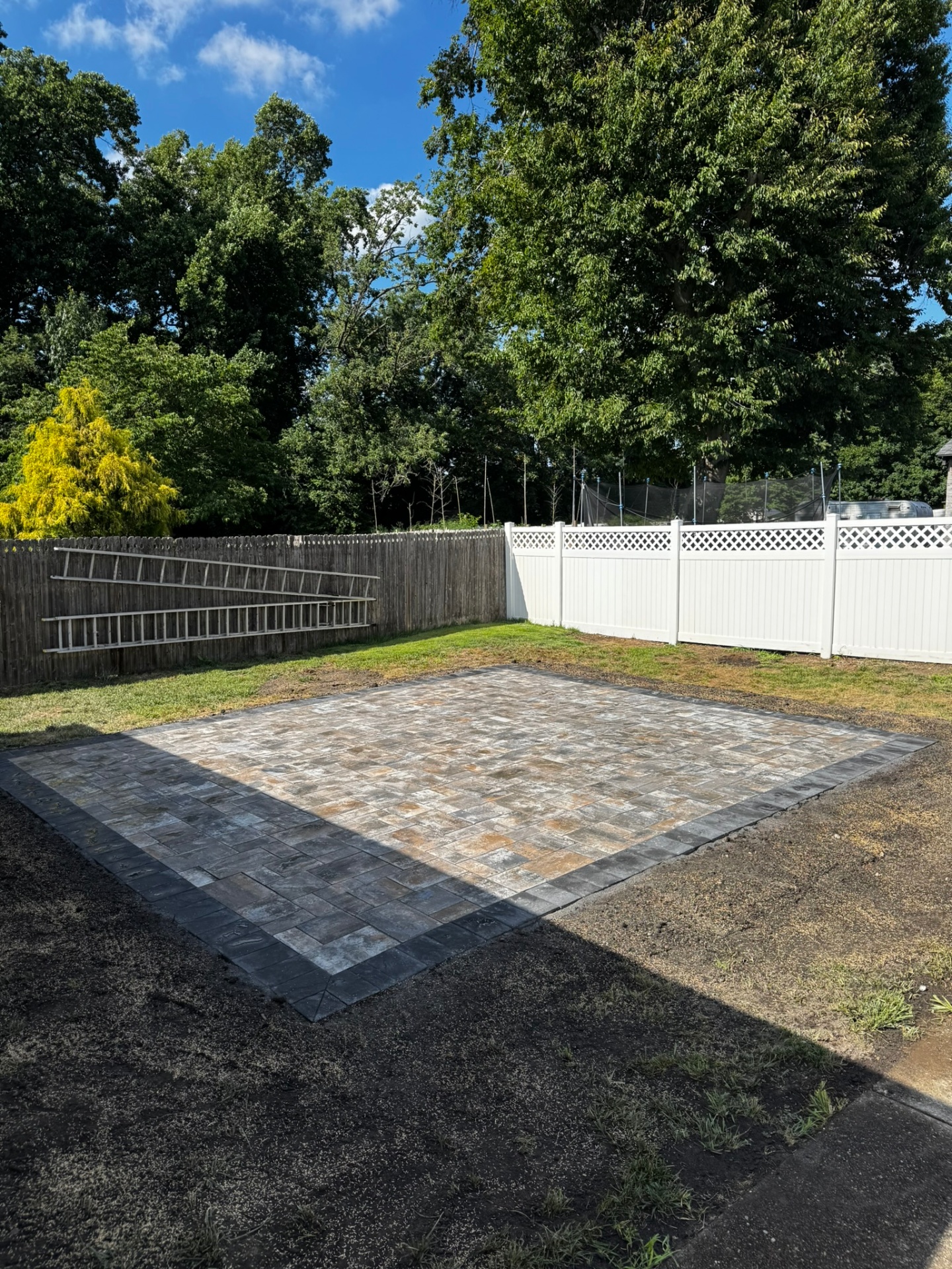 Square paver patio with dark charcoal border in fenced backyard in New Jersey