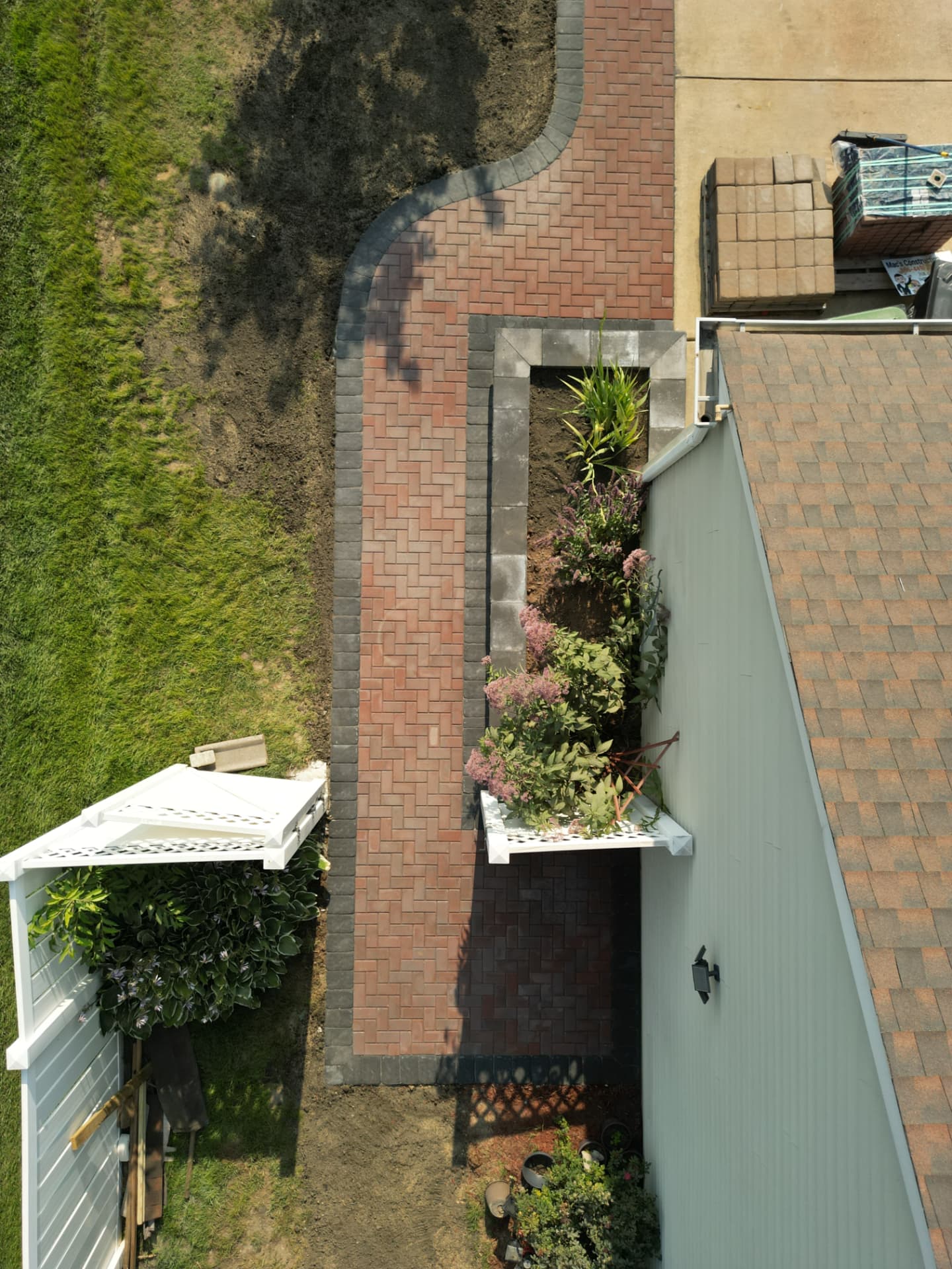Aerial view of a long herringbone brick walkway alongside a raised paver planter wall