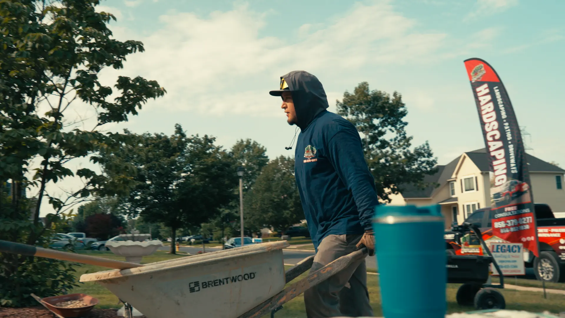 Universal Hardscaping crew member moving a wheelbarrow past the company banner