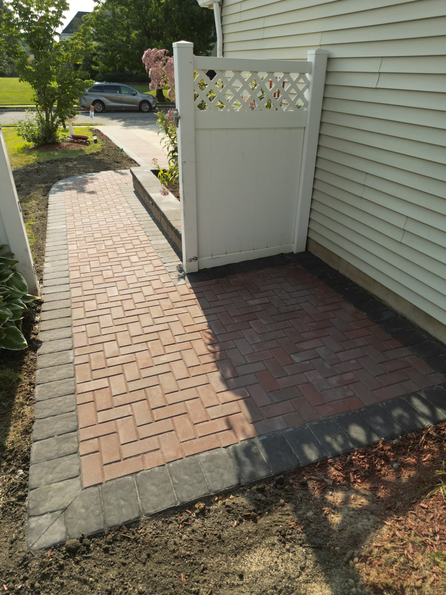Ground view of a red brick paver walkway and herringbone landing at a side gate