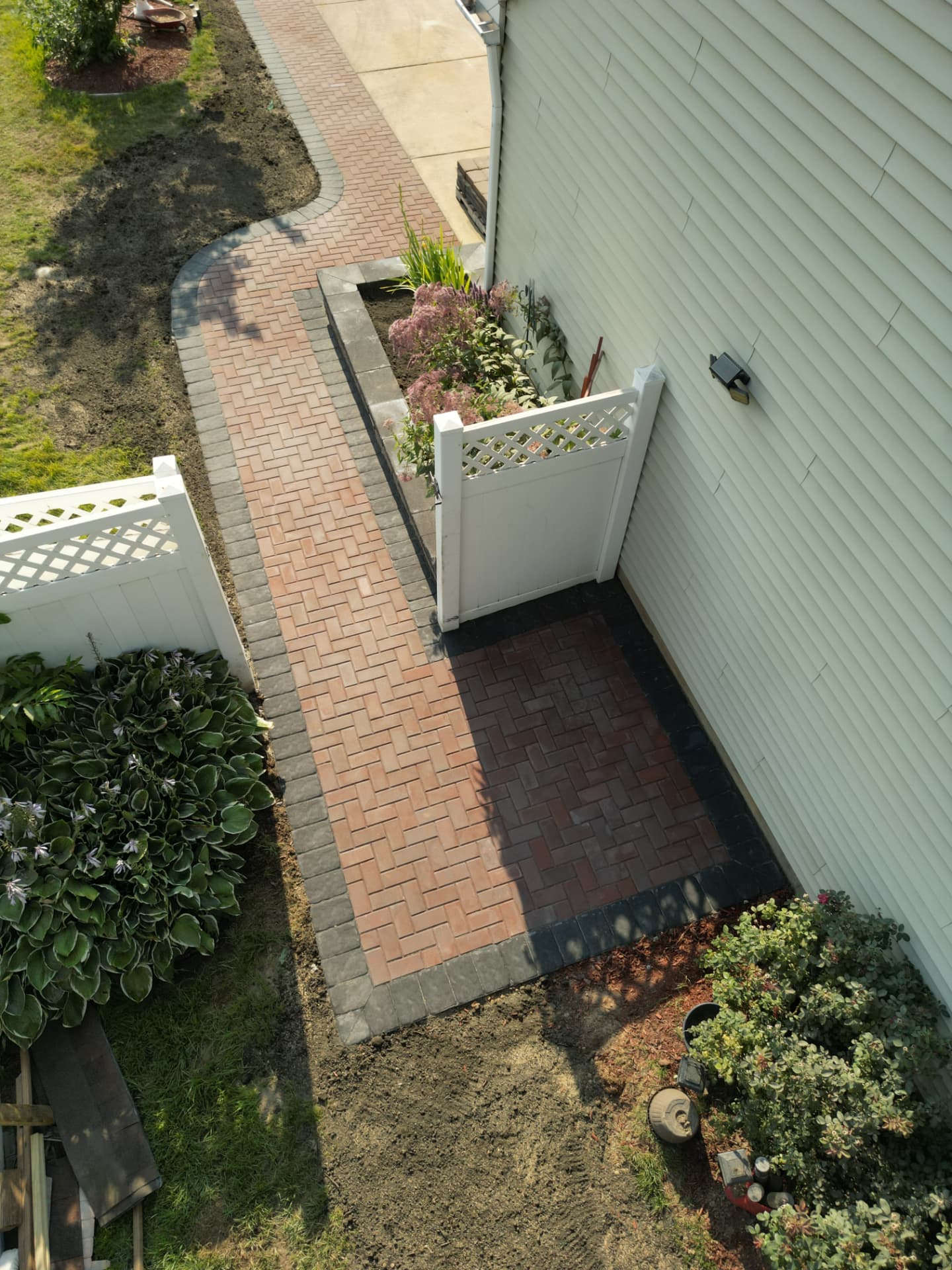 Aerial view of a brick paver side walkway leading to a herringbone landing beside a home
