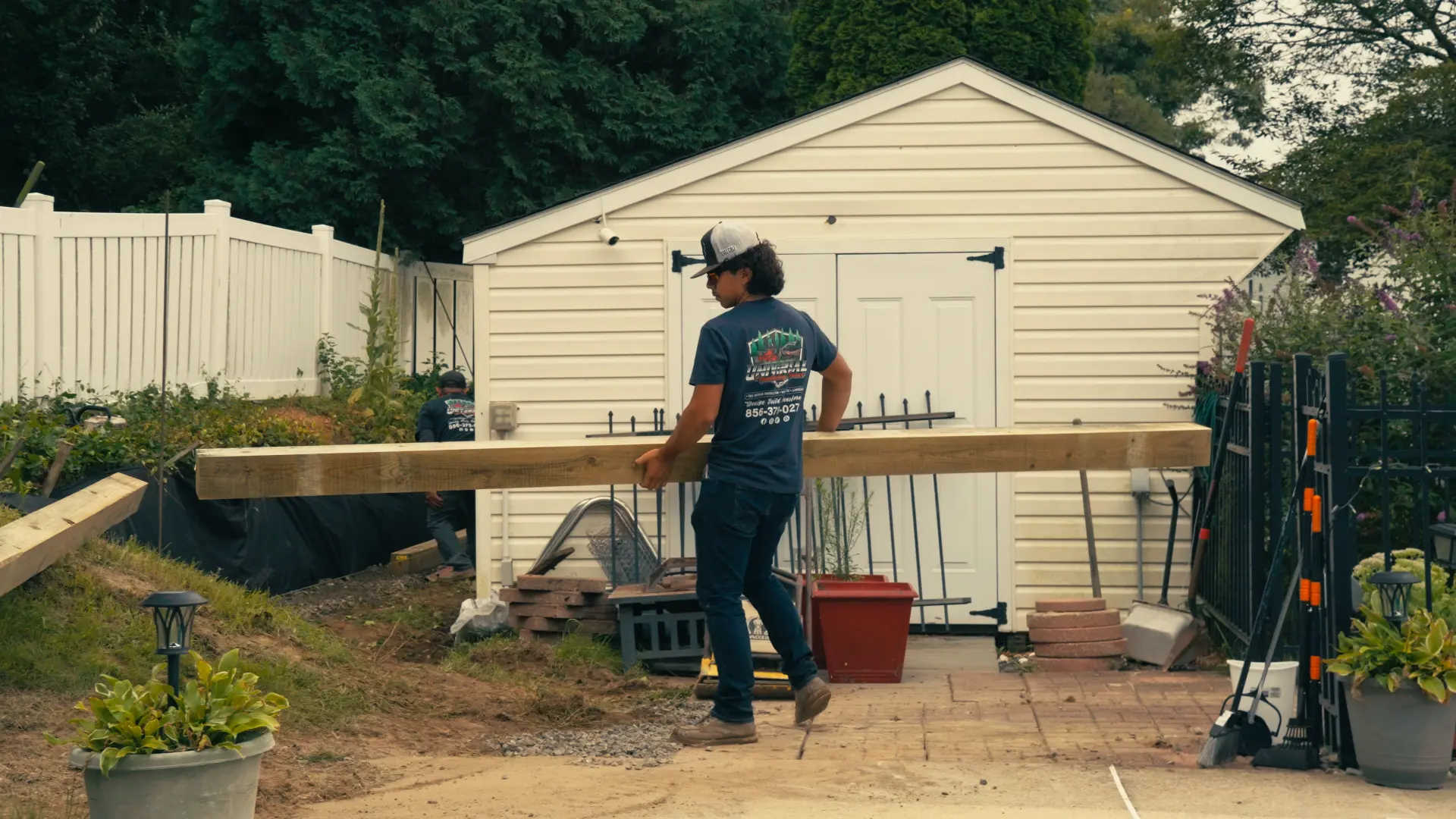 Crew member carrying a pressure-treated timber for a backyard retaining wall