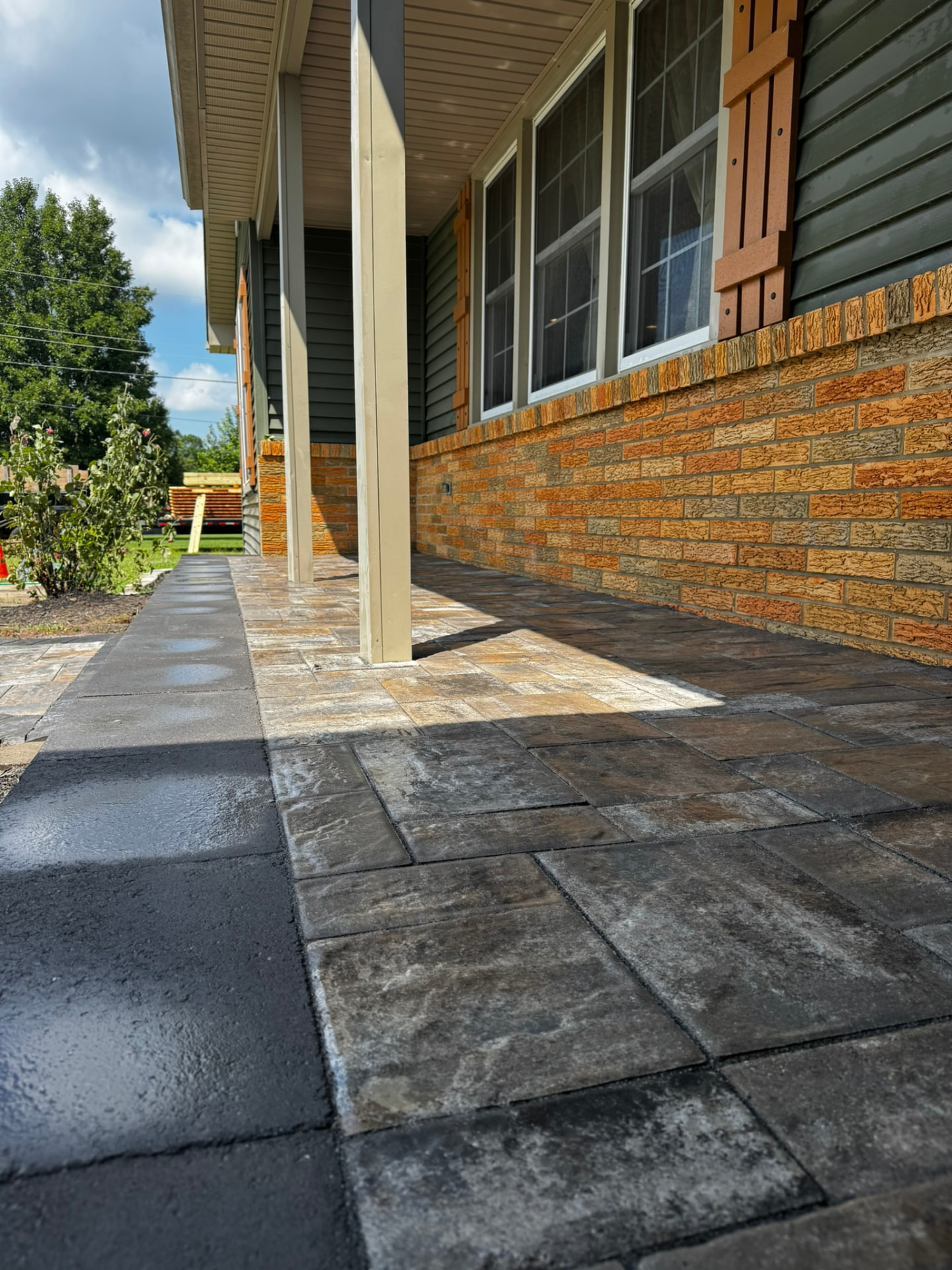 Large-format paver porch and walkway running along a brick and green-sided home in New Jersey