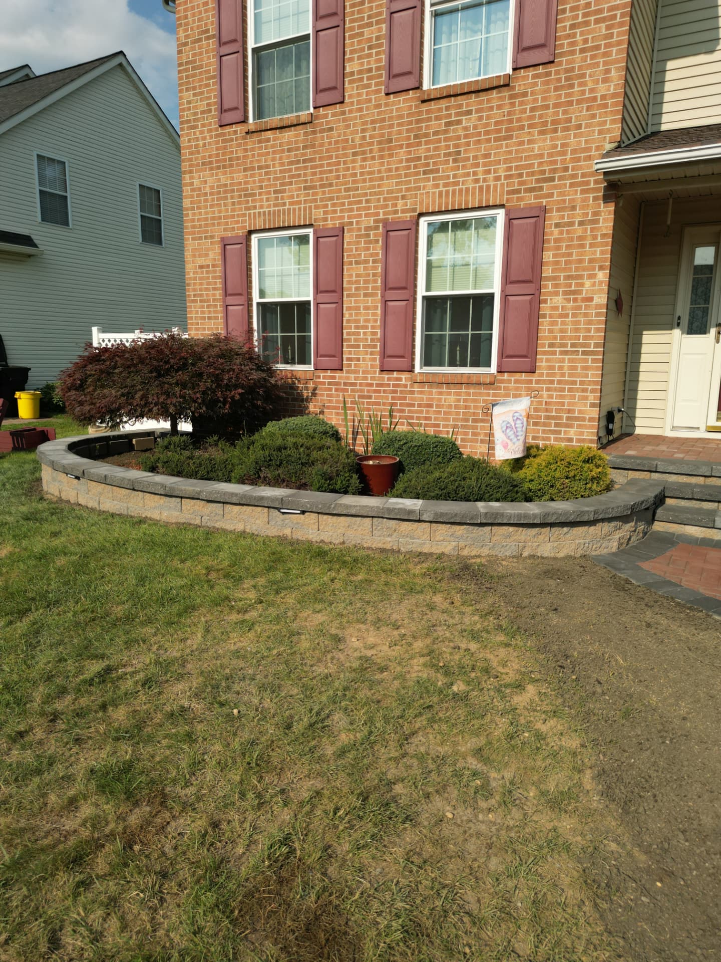 Curved block retaining wall forming a raised front garden bed with shrubs beside a brick home in New Jersey
