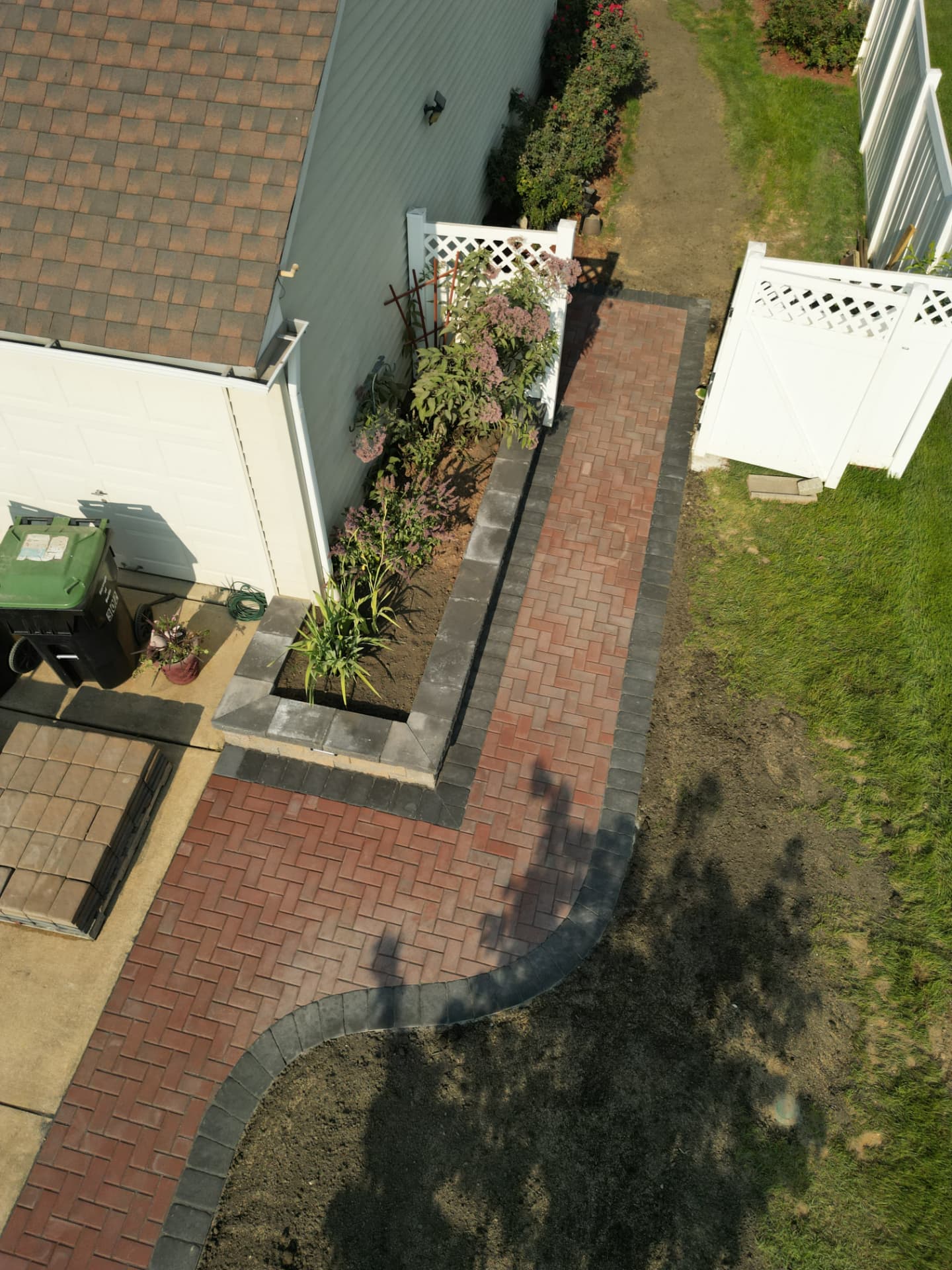 Aerial view of a red herringbone brick paver walkway with charcoal border and raised paver planter bed